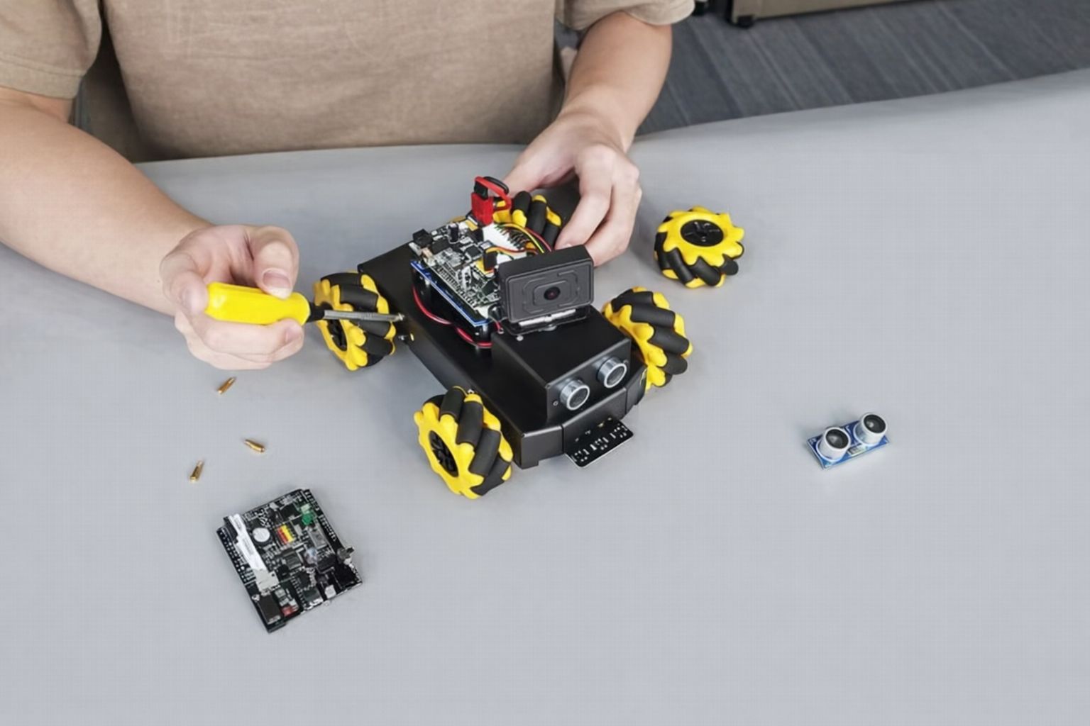 En person monterar en liten utbildningsrobot med en gul skruvmejsel.