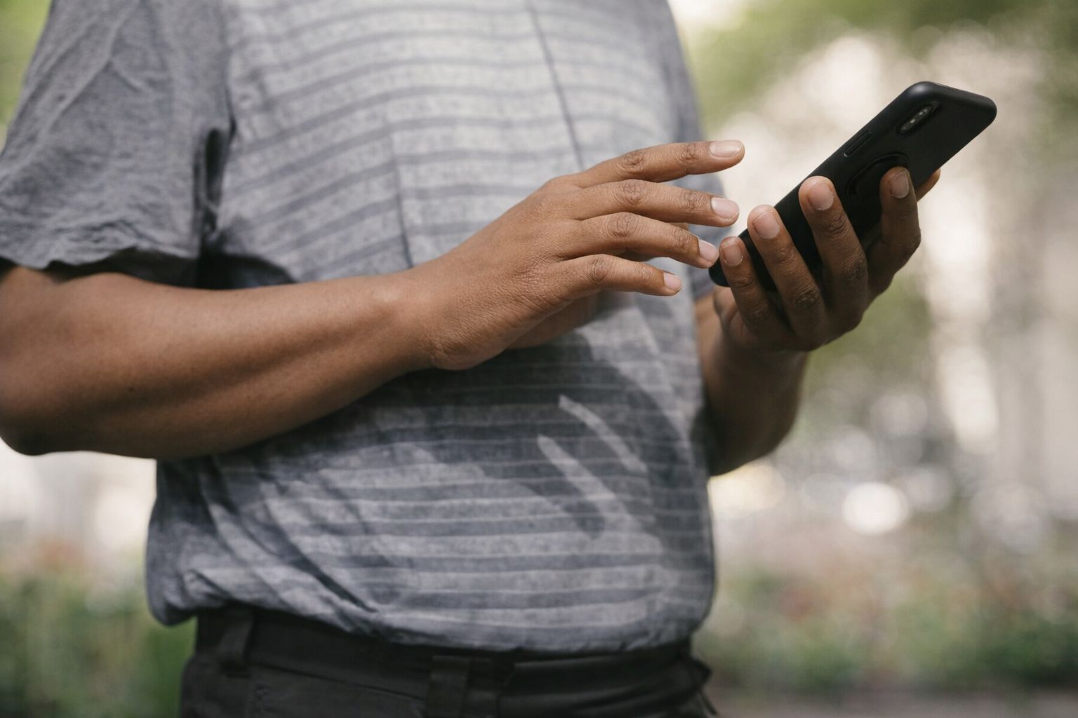 En person i grå tröja använder en mobiltelefon utomhus för att läsa eller skicka information.