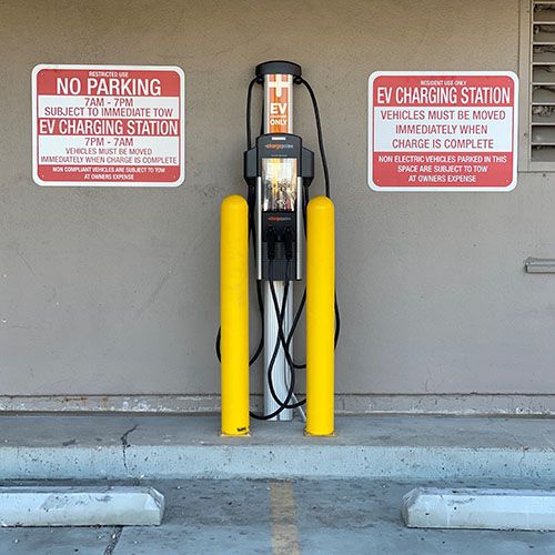 Laddstation för elbilar på en parkeringsplats med varningsskyltar.