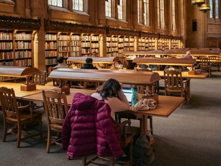 Student studerar ensam vid laptop i ett stort universitetsbibliotek