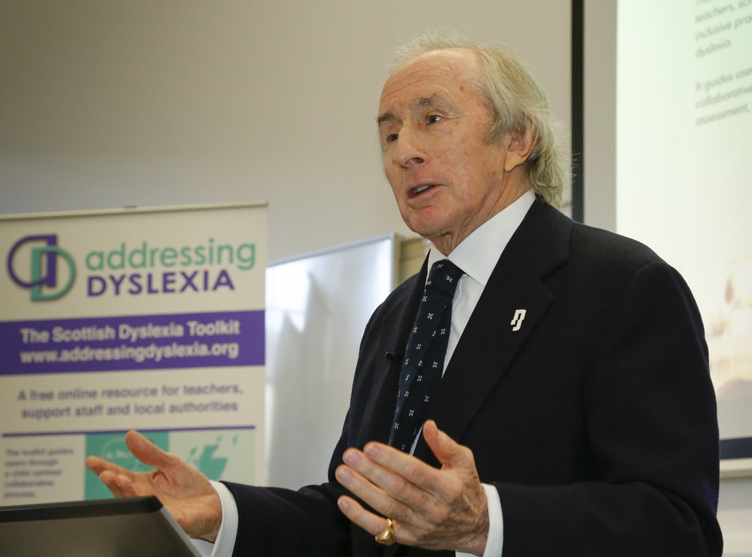 Samma person som i bild 2, från en annan vinkel, presenterar om dyslexistöd med banderollen 'Addressing Dyslexia' synlig.