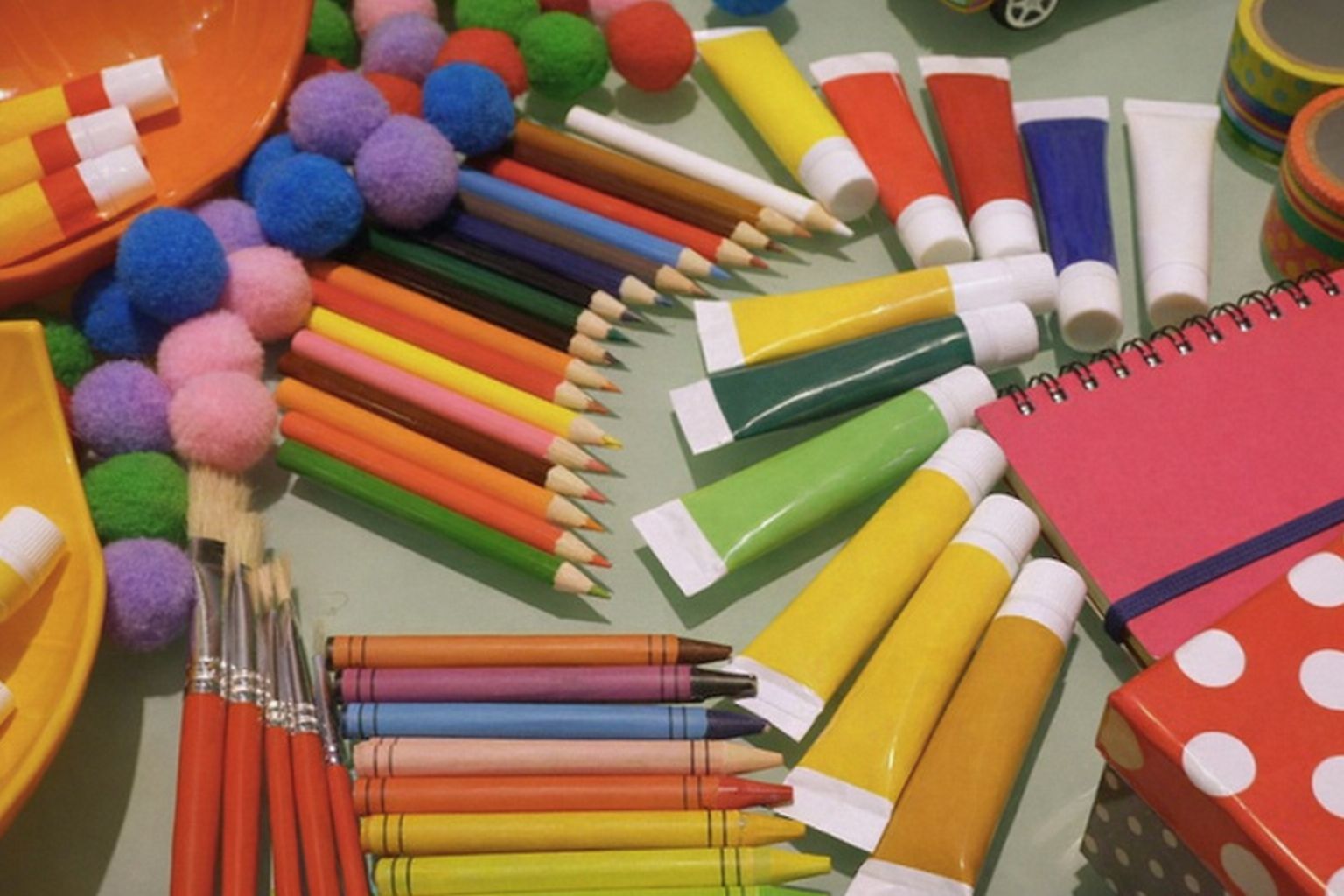 Färgglada skolmaterial som pennor, målarfärg och penslar utspridda på ett bord.